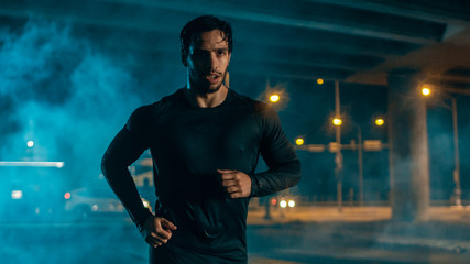 Sweating Tired Athletic Muscular Young Man in Sports Outfit Jogging in a Street Filled With Smoke. He is Running in an Evening Urban Environment Under a bridge.
