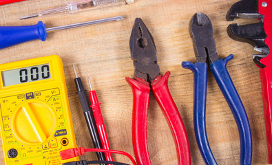 Electrical tester and other tools of electrician on a wooden background.
