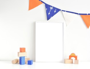 Blank frame for nursery art, white frame mock up, flags bunting with arrows, wooden building blocks.