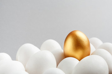 One golden egg among white eggs on gray background.