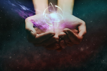 Human hand holding atom on a palm. Nebula dust in infinite space. Mixed media.