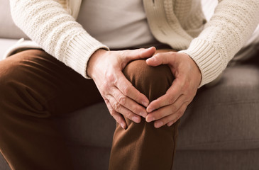 Mature man suffering from knee pain on sofa