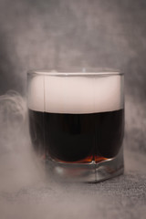 glass of dark liquid and smoke around on a gray background