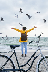 back view to a young female standing with a bicycle on the beach with raised hands surrounded with...