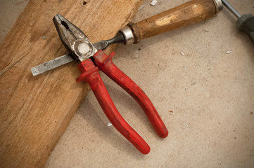 Obraz premium A metallic chisel and pliers with red handle on the wooden board