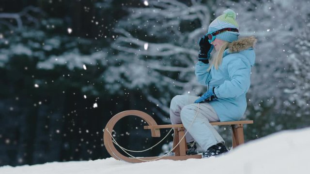 CINEMAGRAPH - SEAMLESS LOOP. Cute little girl child preparing for a sledge ride down the hill. Child plays outdoors in snow, winter fun. 4K UHD