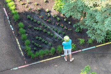 Unknown man watering a flower garden with a hose