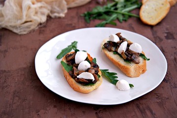 Light snack, crispy bruschetta with champignons, arugula and mozzarella. Italian Cuisine.