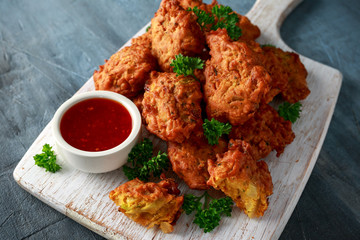 Crispy onion bhajis with sweet chilli sauce on white wooden board
