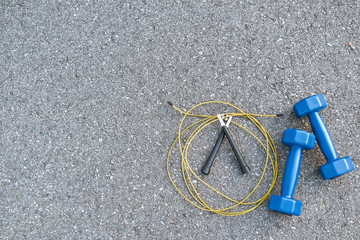 Jump rope and two blue lightweight dumbbells are lying at asphalt