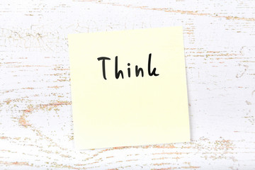 Yellow sticky note on wooden desk with handwritten text think
