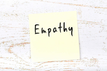 Yellow sticky note on wooden desk with handwritten text empathy