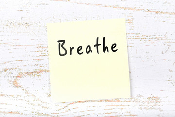 Yellow sticky note on wooden desk with handwritten text breathe