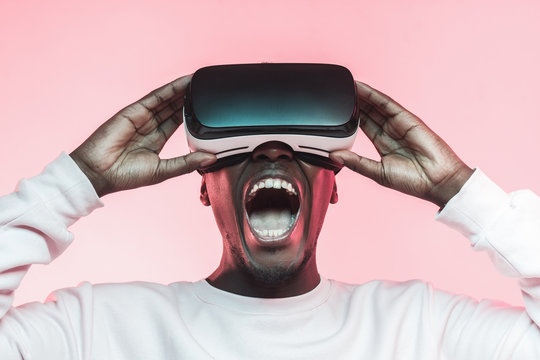 Young screaming african man experiencing virtual reality with VR headset, isolated on pink background