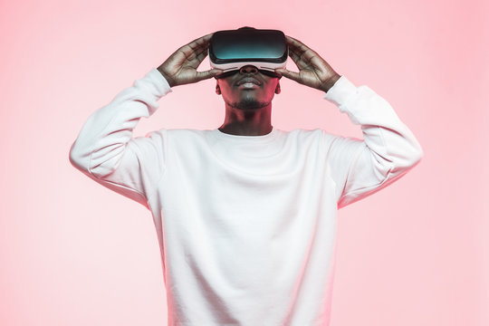 Young african man holding virtual reality goggles with both hands, isolated on pink background - Powered by Adobe