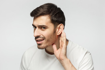 Man isolated on gray background pressing hand to ear trying to hear something better
