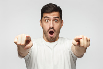 European male pointing at camera with both hands with amazed and shocked face as if surprised with...