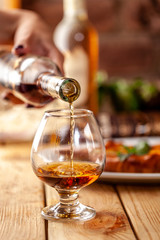 Concept of Georgian restaurant. A girl pours Georgian brandy from a bottle into a glass. On a...