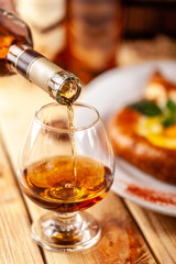 Concept of Georgian restaurant. A girl pours Georgian brandy from a bottle into a glass. On a wooden table is hachipuri
