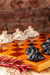 concept of Georgian cuisine. black and white khinkali stand on a chessboard. female hand takes khinkali. khinkali with barinas, veal and cheese.