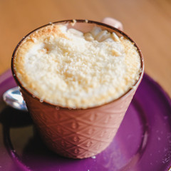 Mug of brown cacao decorated with nut crumb on a wooden table.