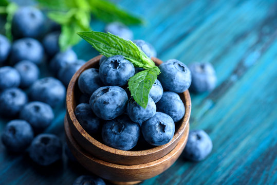 Bowl of fresh blueberries on blue rustic wooden table closeup.