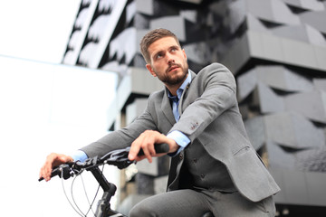 Handsome young businessman riding bicycle outdoors in the city.