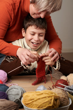 Mother is learning her child boy to knit. Colorful wool yarns are on the wooden table.