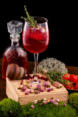 Vertical image of glass with wine alcohol cocktail decorated with cranberry, rosemary and rose flowers at wooden table background.