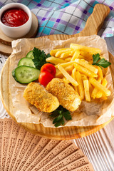 Vertical  image of nuggets with vegetables, fried potato and ketchup on wooden tray at decorated table background.