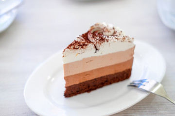 Piece of triple chocolate mousse cake on a white plate in cafe. Sweet dessert concept.