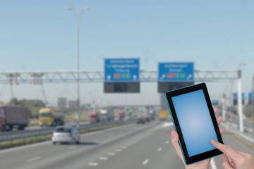 Riding a highway  infographic concept. Finger touching tablet blue blank screen ready for your text. Intentionally blurred image of a motorway in the background. All potential trademarks are removed