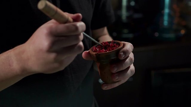 Preparation of hookah, a man's hand puts fruit-flavoured tobacco in the bowl of a shisha. Close-up of a man preparing fruit tobacco in a bowl for a hookah in a bar on a black background. Slow motion.