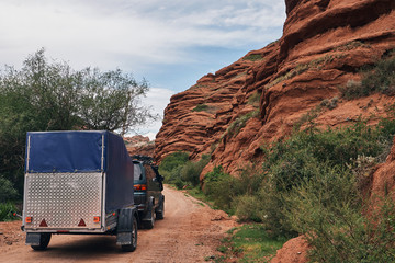 A car with a trailer is driving along the Amazing Red Mountain range of Jeti Oguz (Seven bulls Rock...