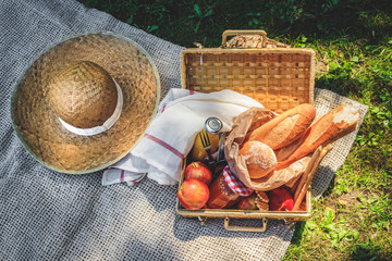 Hat, straw basket with food and drinks on beige plaid .