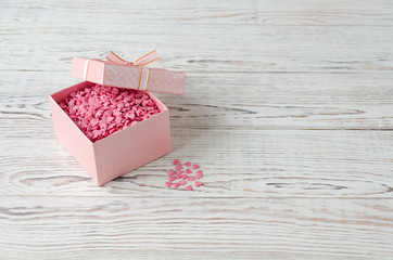 Pink box with small hearts on white wooden background.