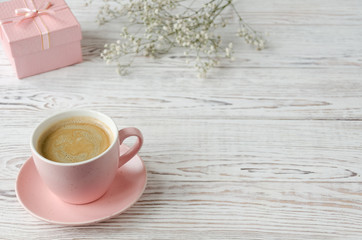 Cup of coffee, pink box and gypsophila on white wooden background.