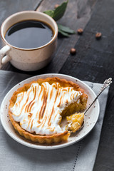 Hand made tart, tartlet with lemon curd and meringue and cup of coffee on a black wooden background. Selective focus, top view