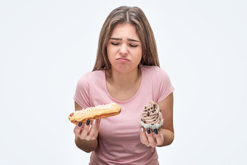 Upset young woman look at eclair and cake. She feel sickness. Isolated on white background.