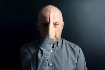 Obraz premium Bearded man shielded half of his face from the light with his palm