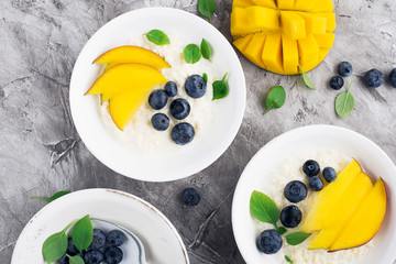 Milk porridge for breakfast with slices of mango and fresh blueberries. Top view.