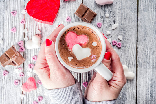 Girl hands hold little heart shaped gift box, old wooden table with hot chocolate with marshmallow hearts and tulip flowers, Valentine day background copy space top view, hands in picture flatlay
