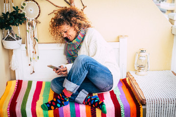 Cheerful happy woman sit down at home on a bench outdoor terrace reading and using modern phone for...