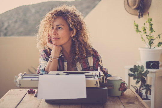 beautiful happy relaxed middle age caucasian woman blonde curly hair taking a break and stop writing with her old typewriter - blogger writer work and hobby time for hipster cheerful modern woman