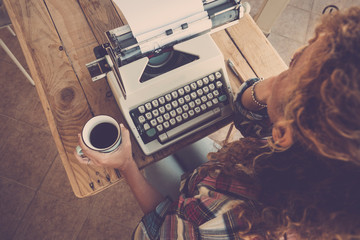 Above view of curly woman thinking and taking coffee with old typewriter on the table ready to...