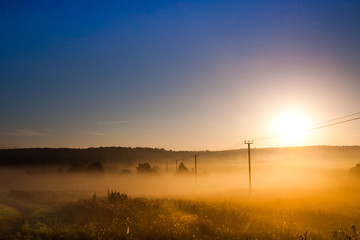 Fototapeta na wymiar Dawn, the morning sun rises over the field and power transmission line, misty dawn landscape