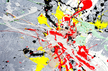 a spot of white and black and yellow and green and red spilled paint on a concrete textured surface