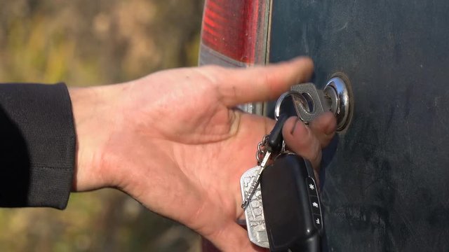 A man closes or opens the trunk of the car with a key