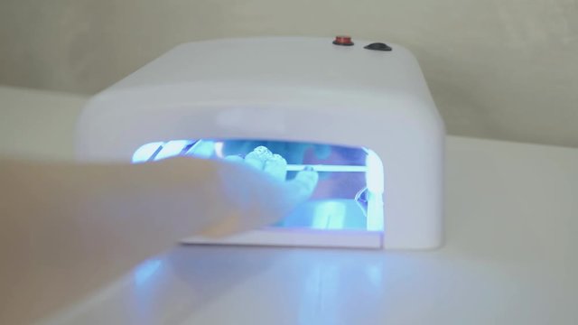 Woman dries her nails with shellac in UV lamp. Close-up.