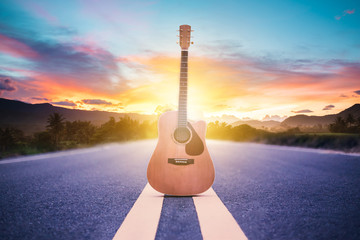 Wooden acoustic guitar lying on street with sunrise background, journey of musician concept